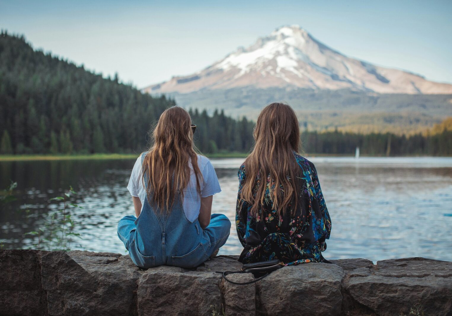 women sitting on rock near body of water